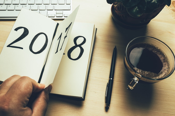 New Year 2018 is coming concept. Hand flips notepad sheet on wooden table. 2017 is turning, 2018 is opening 2017