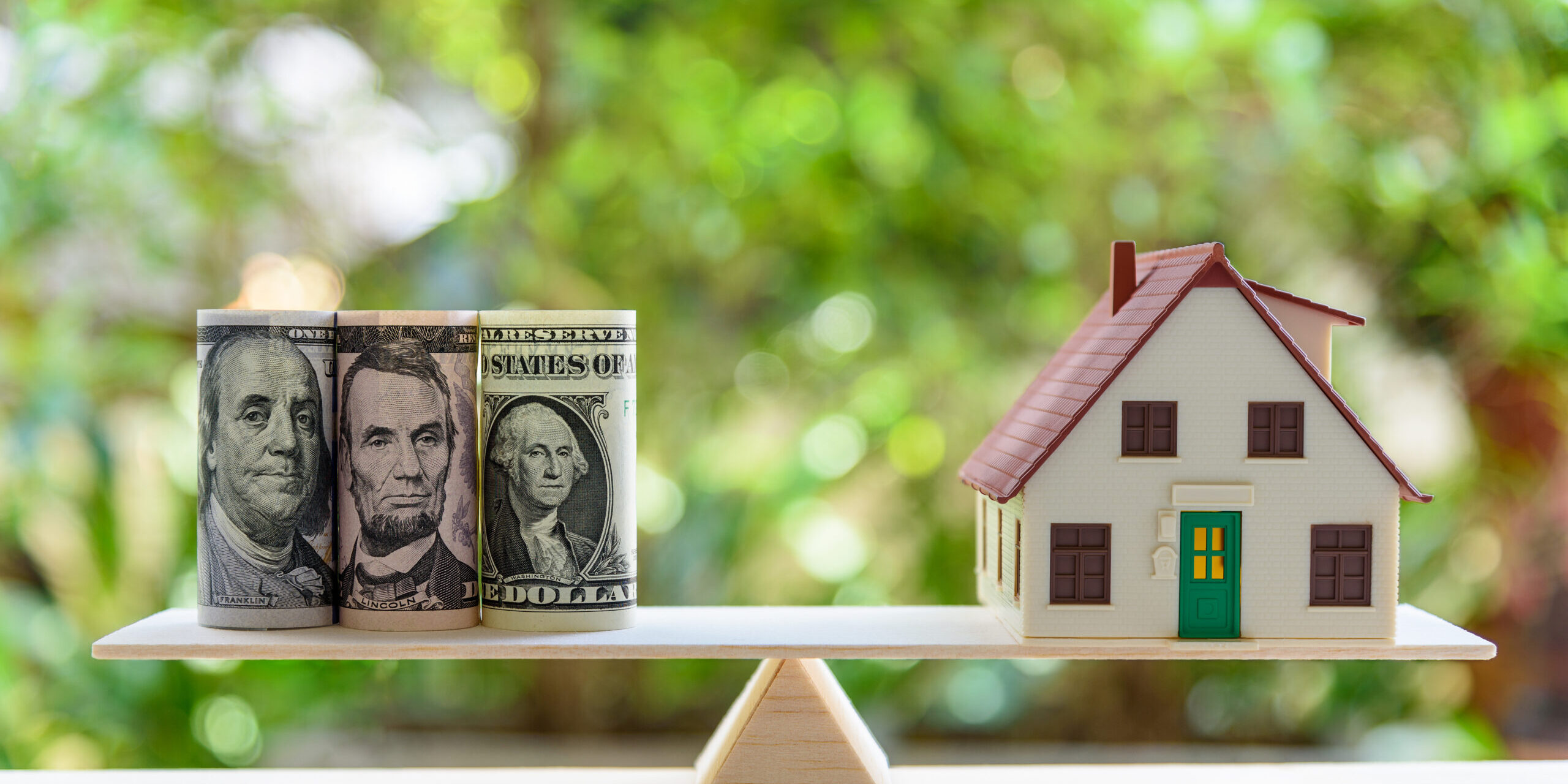 Home loan / reverse mortgage or transforming assets into cash concept : House model, US dollar notes on a simple balance scale, depicts a homeowner or a borrower turns properties / residence into cash