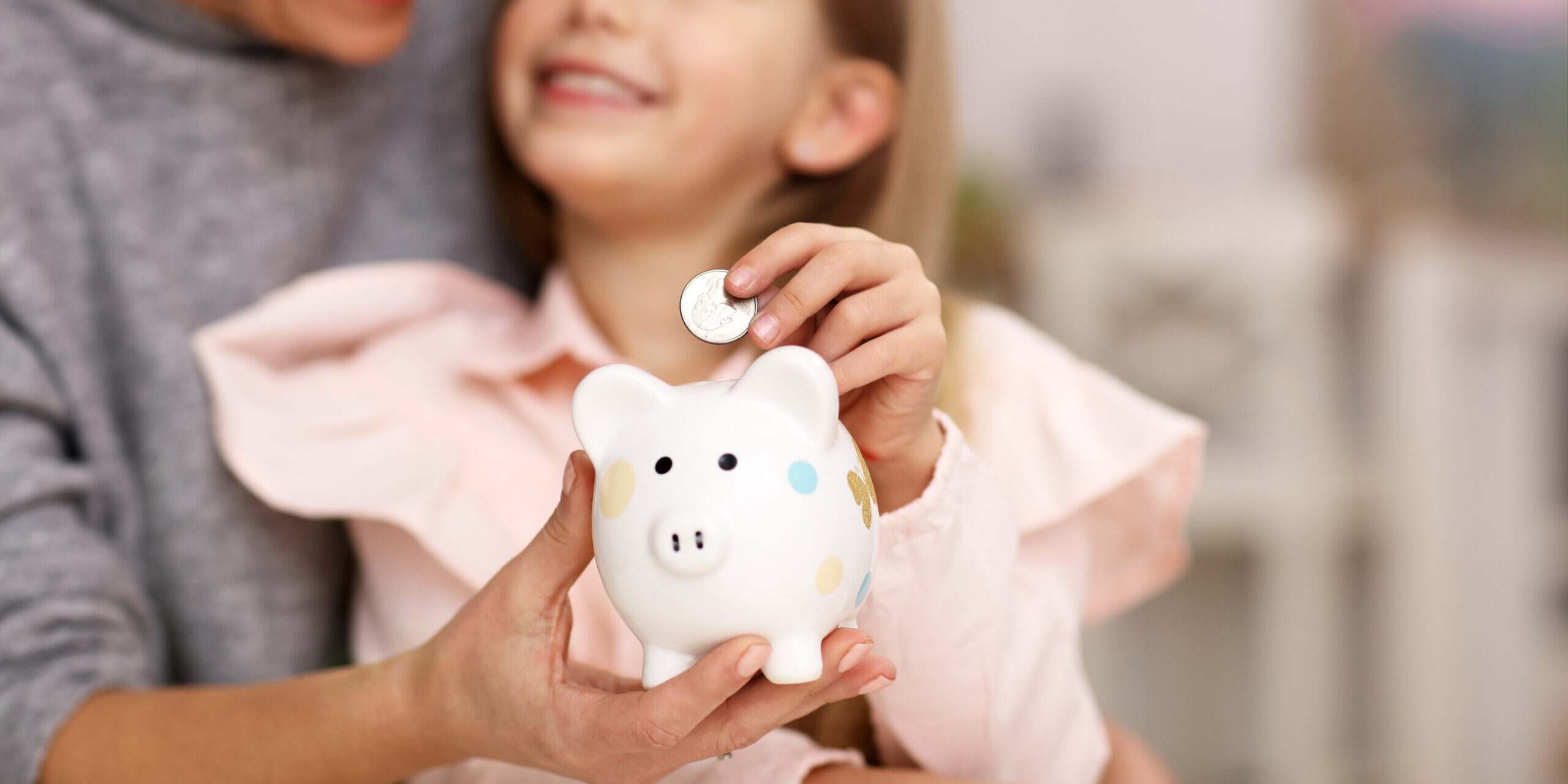 Young girl and her mother with piggybank sitting at table