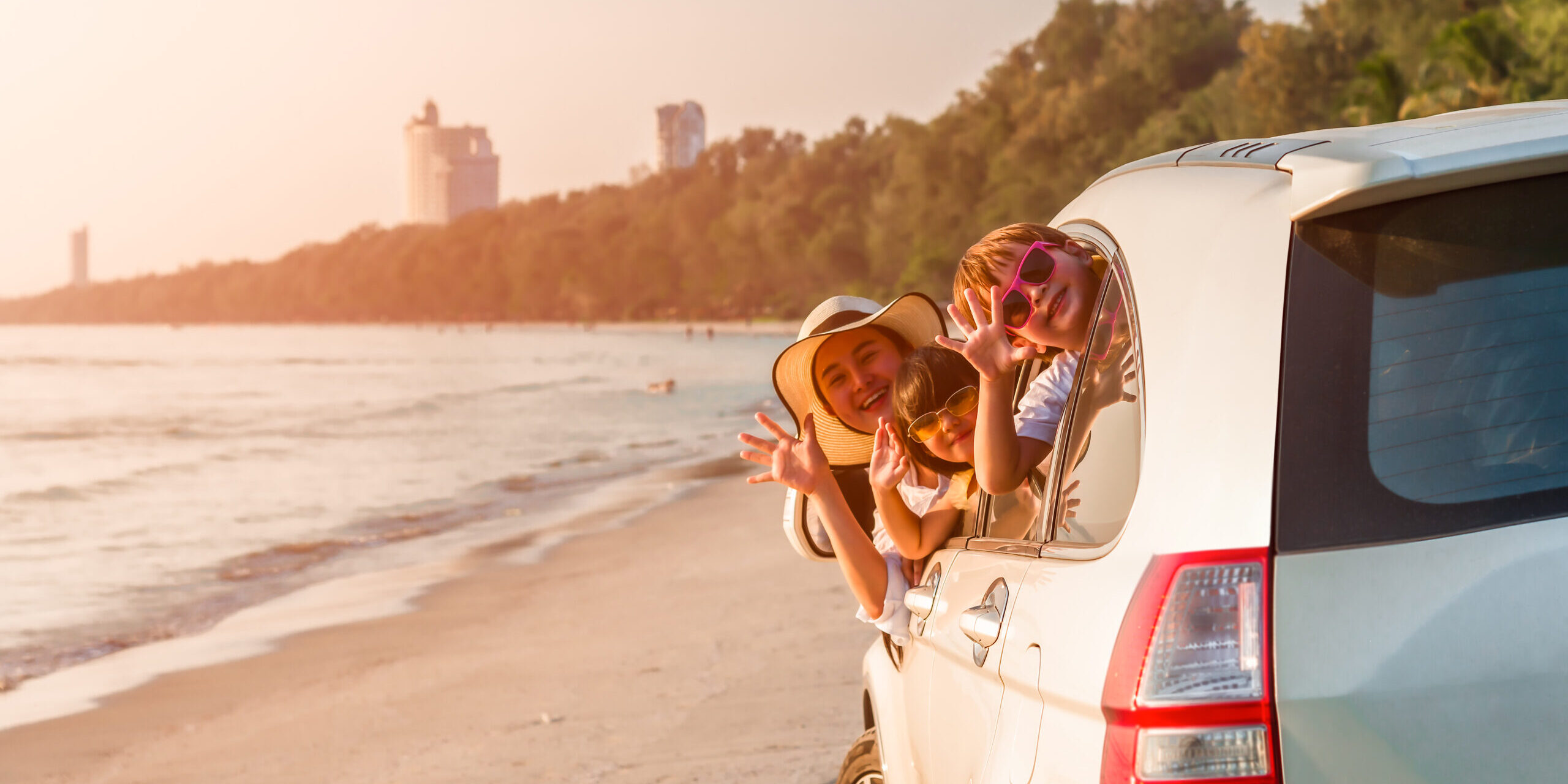 Happy family young woman with her daughter and son sitting in white car with hand up and look out from windows