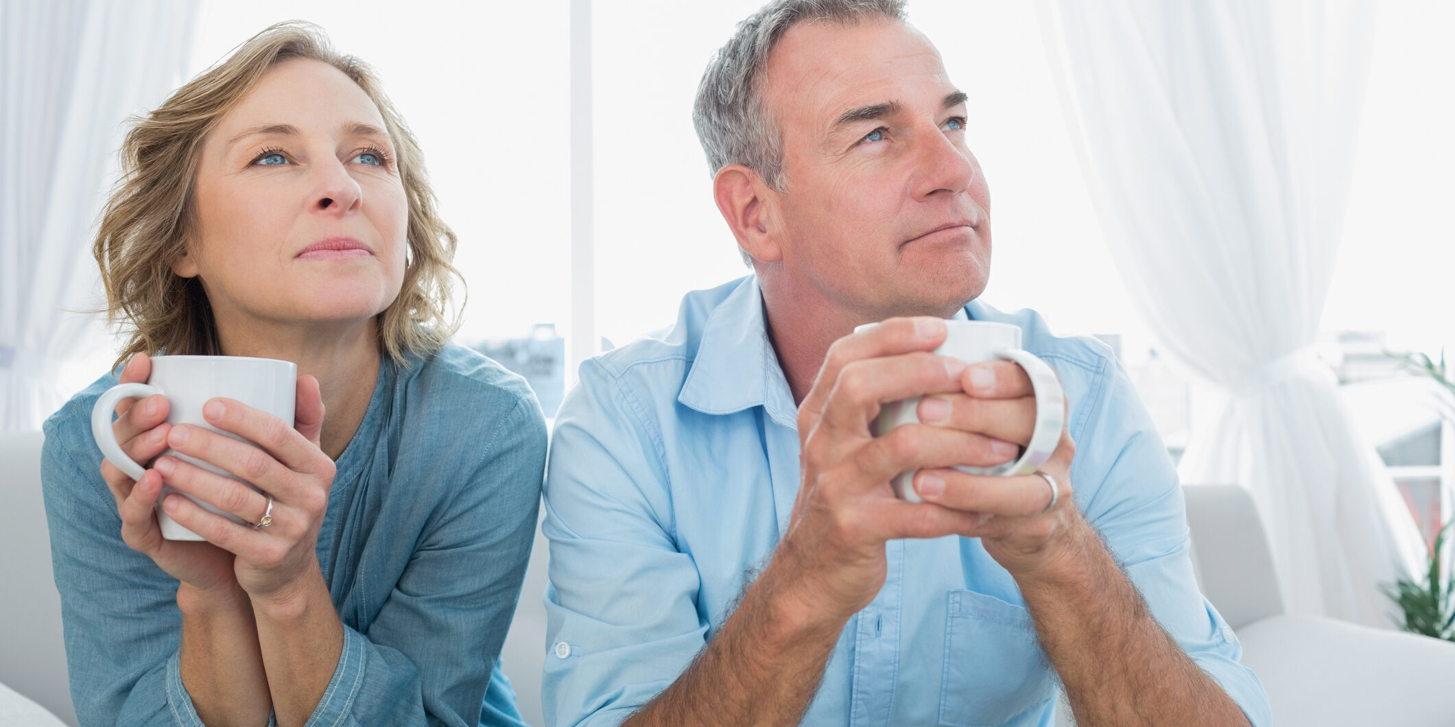 Thoughtful middle aged couple sitting on the couch having coffee