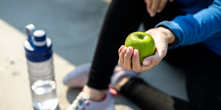 Healthy woman hold apple fruit and sitting on the ground.