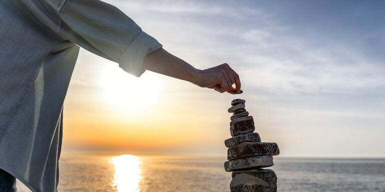 Woman building a cairn pyramide on the seashore at sunset. Zen relaxation and meditation concept