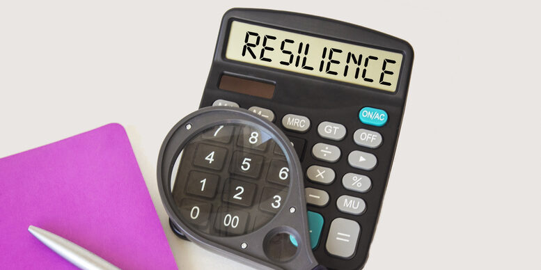 Resilience, text written on a calculator, next to a notepad, a magnifying glass and a pen on a white background.